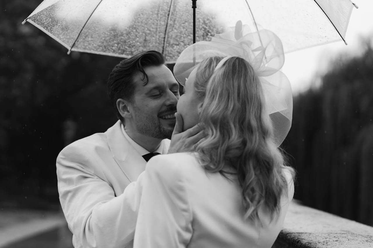 Anna und Marco küssen sich im Regen unter einem transparenten Schirm