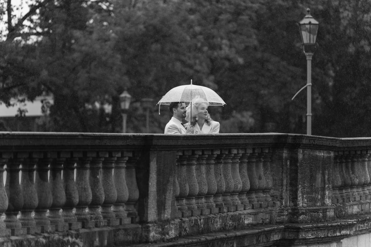 Anna und Marco unter dem Regenschirm auf einer Terrasse mit Balustrade
