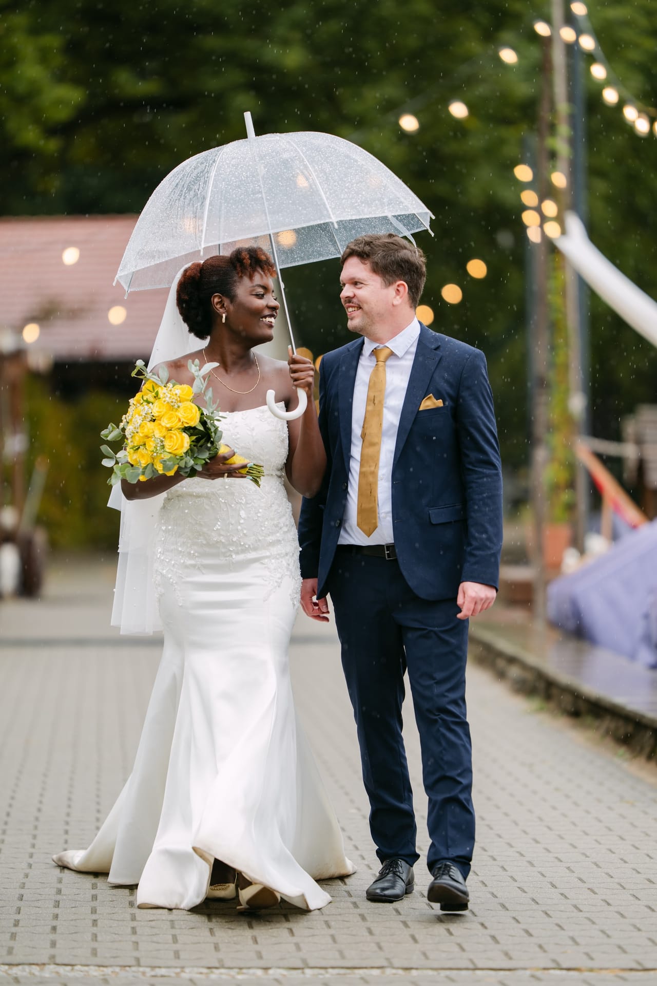 Martha und Volker gehen unter einem Regenschirm, Lichterketten im Hintergrund